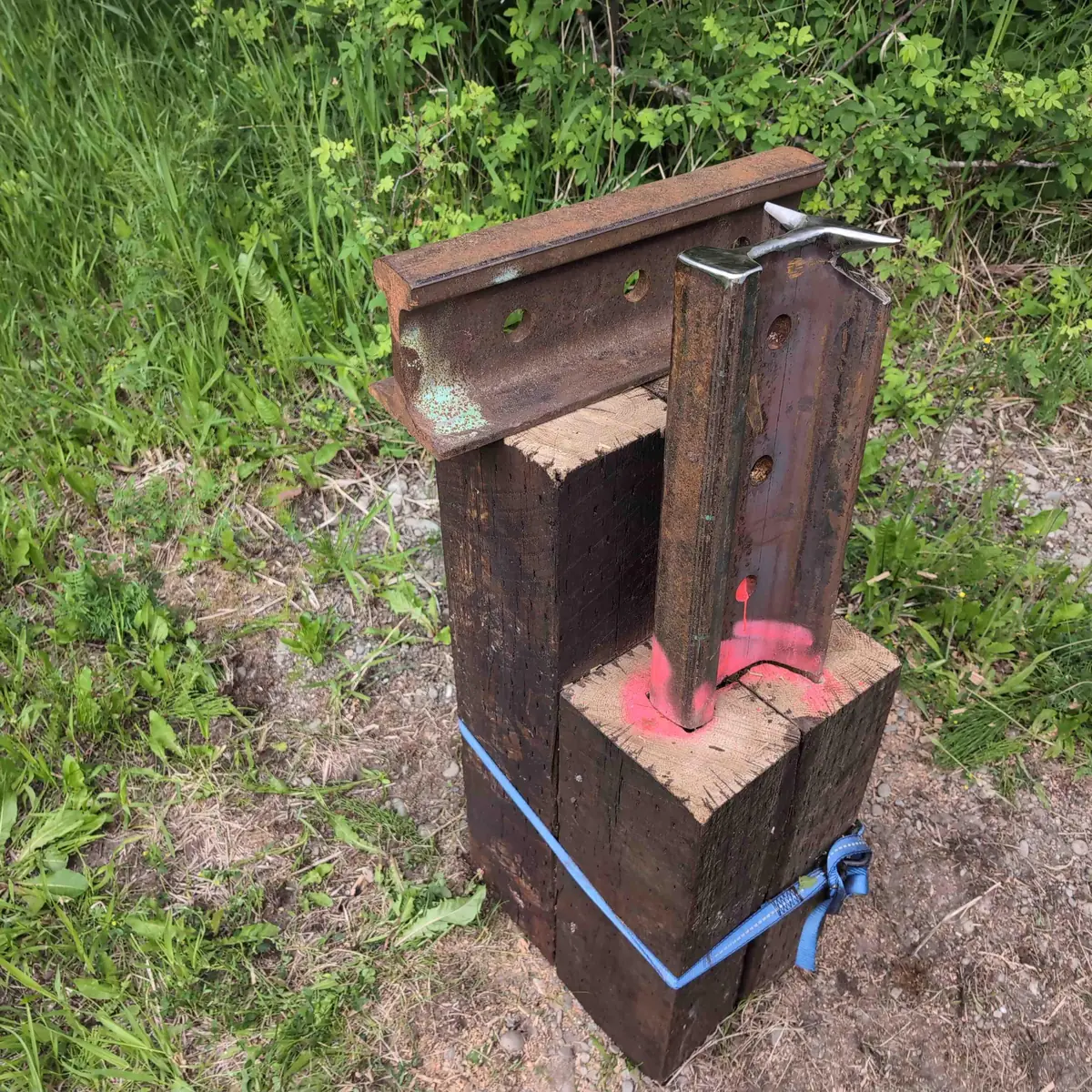 A vertical rail anvil and a horizontal rail cutting station arranged on top of a two-tier anvil stand made out of rail ties fastened together with chain.