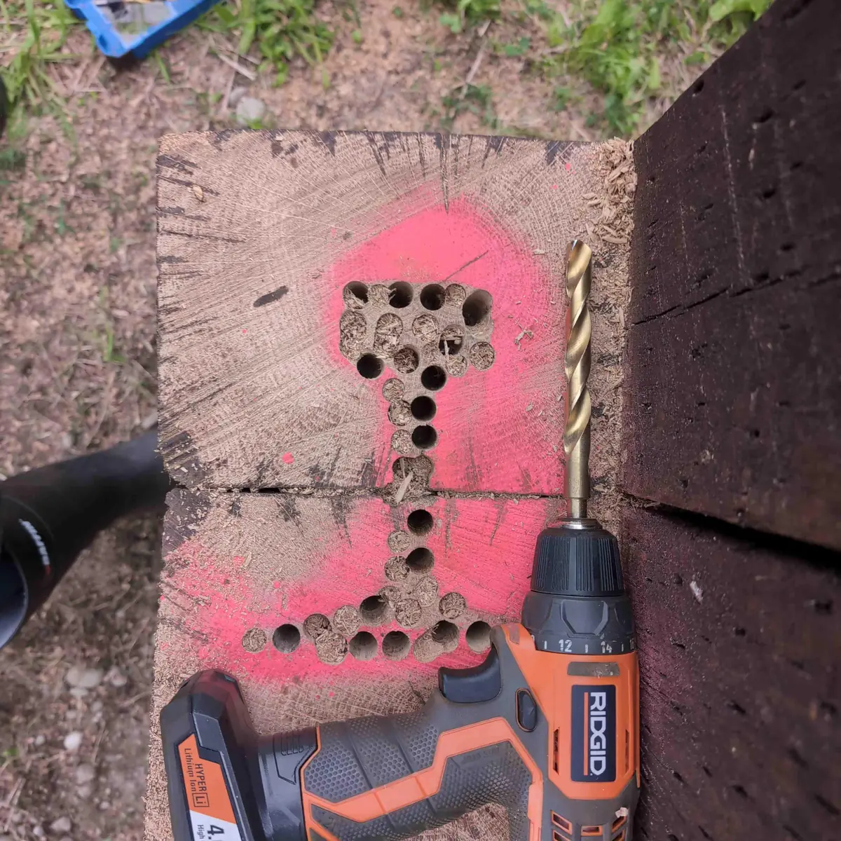 A Ridgid 12v drill next to a bunch of holes drilled out of an outline.