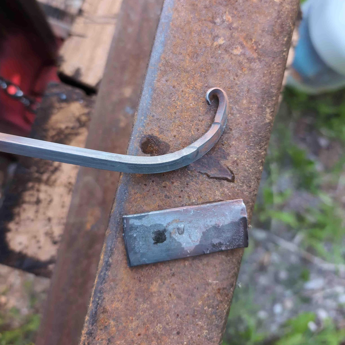 A piece of 1/4 inch square bar with a small taper and curly bit on the end, next to a cut off piece of 1 inch flat stock.